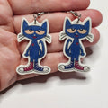 Pete the Cat character earrings with silver dangle hardware held by a hand. 