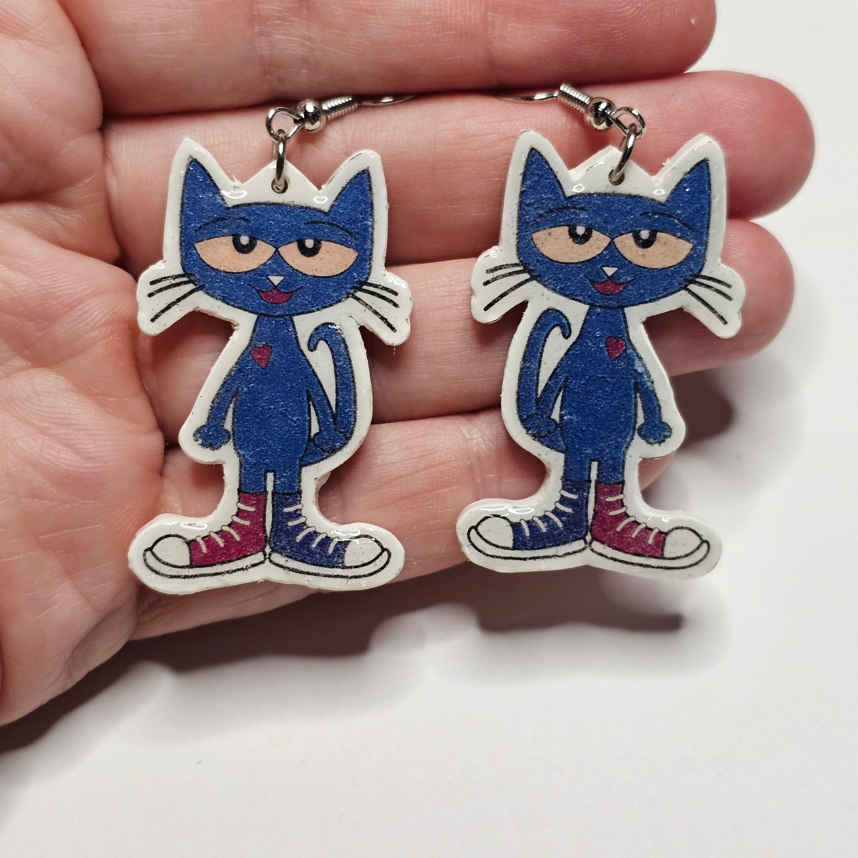 Pete the Cat character earrings with silver dangle hardware held by a hand. 