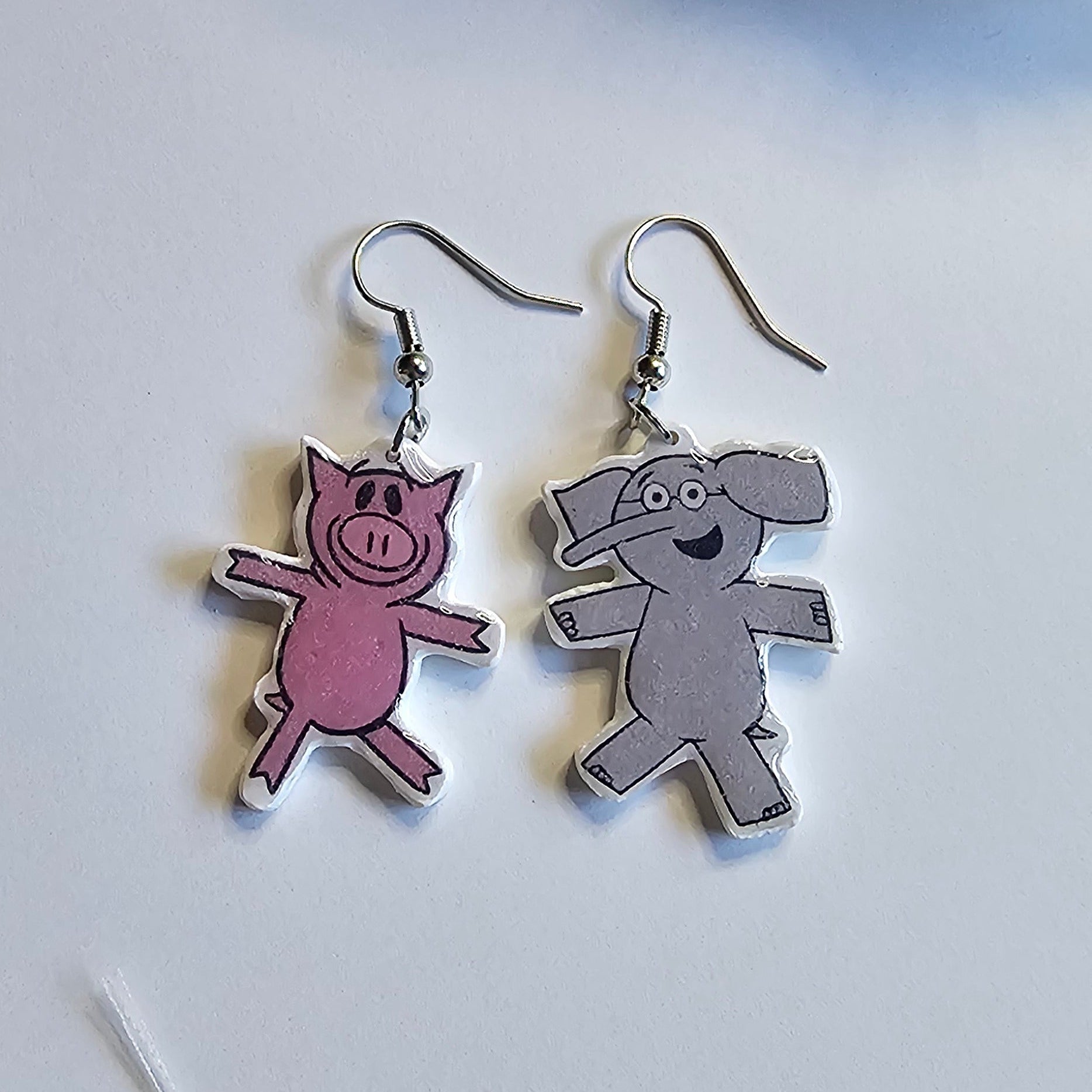 Piggy and Elephant dangle silver dangle earrings made out of polymer clay on a white background. 