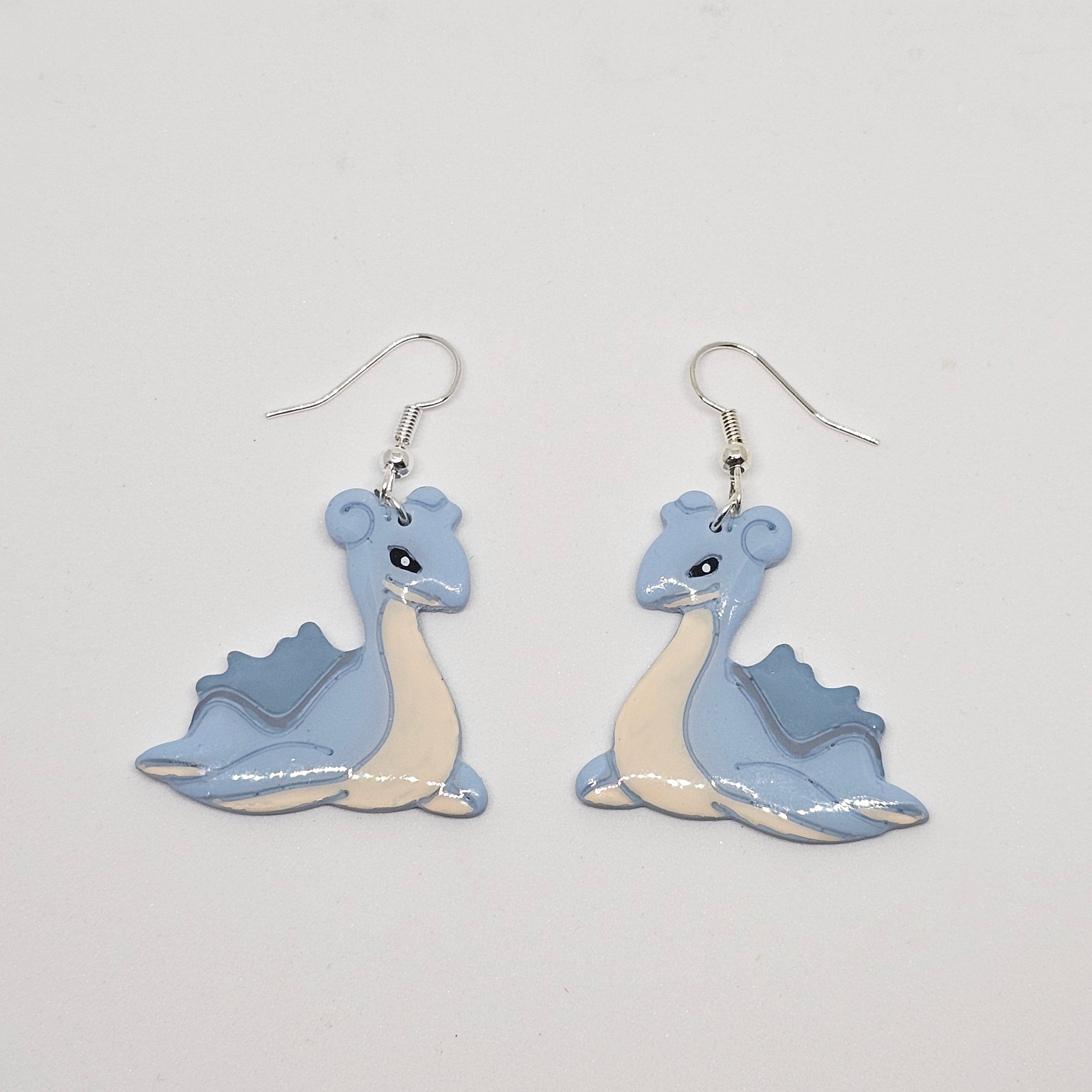 White gold dangle earrings of pokemon Lapras made out of polymer clay.