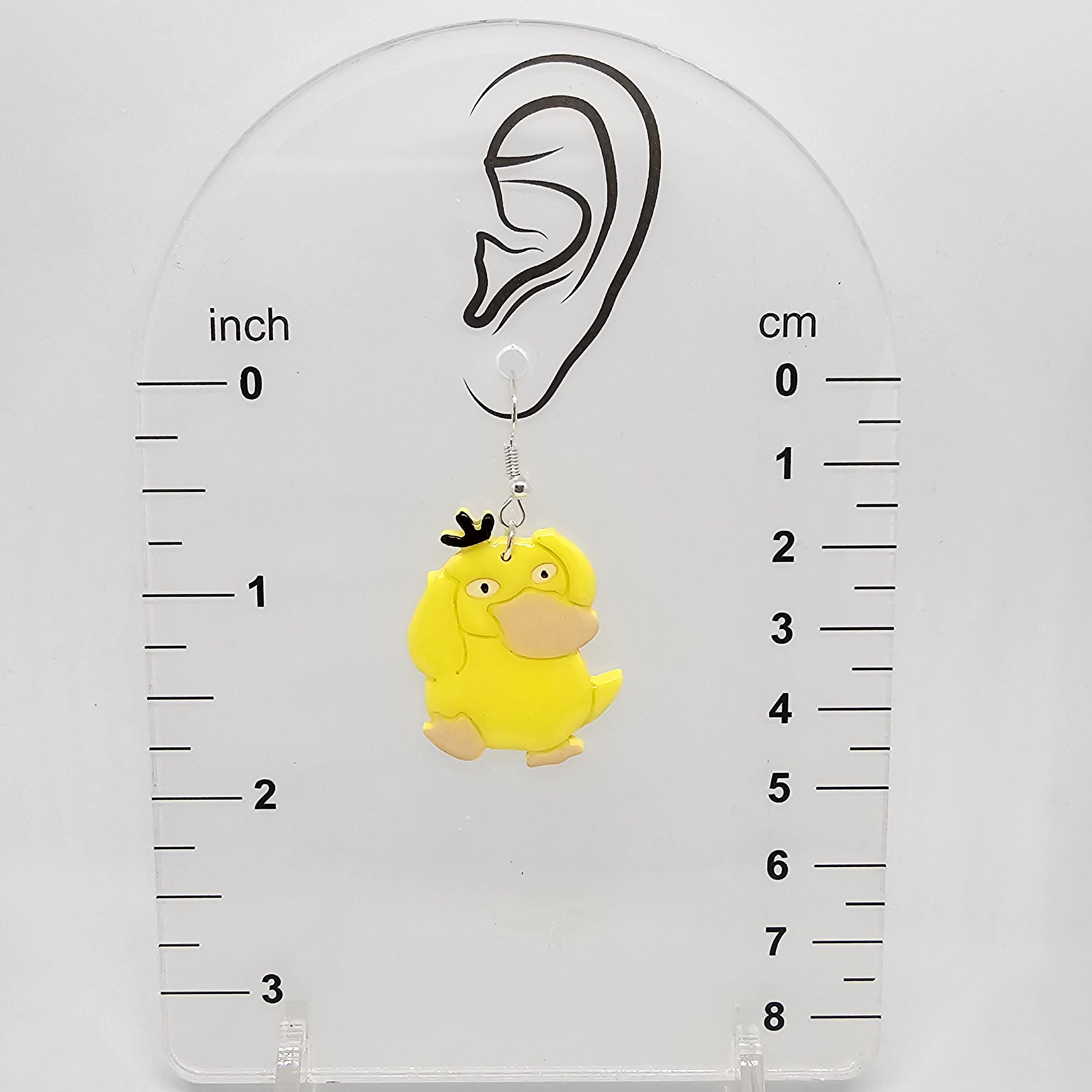 Psyduck earring on an earring device holder showing the earring dangles down about 1.75in from ear lobe hole.