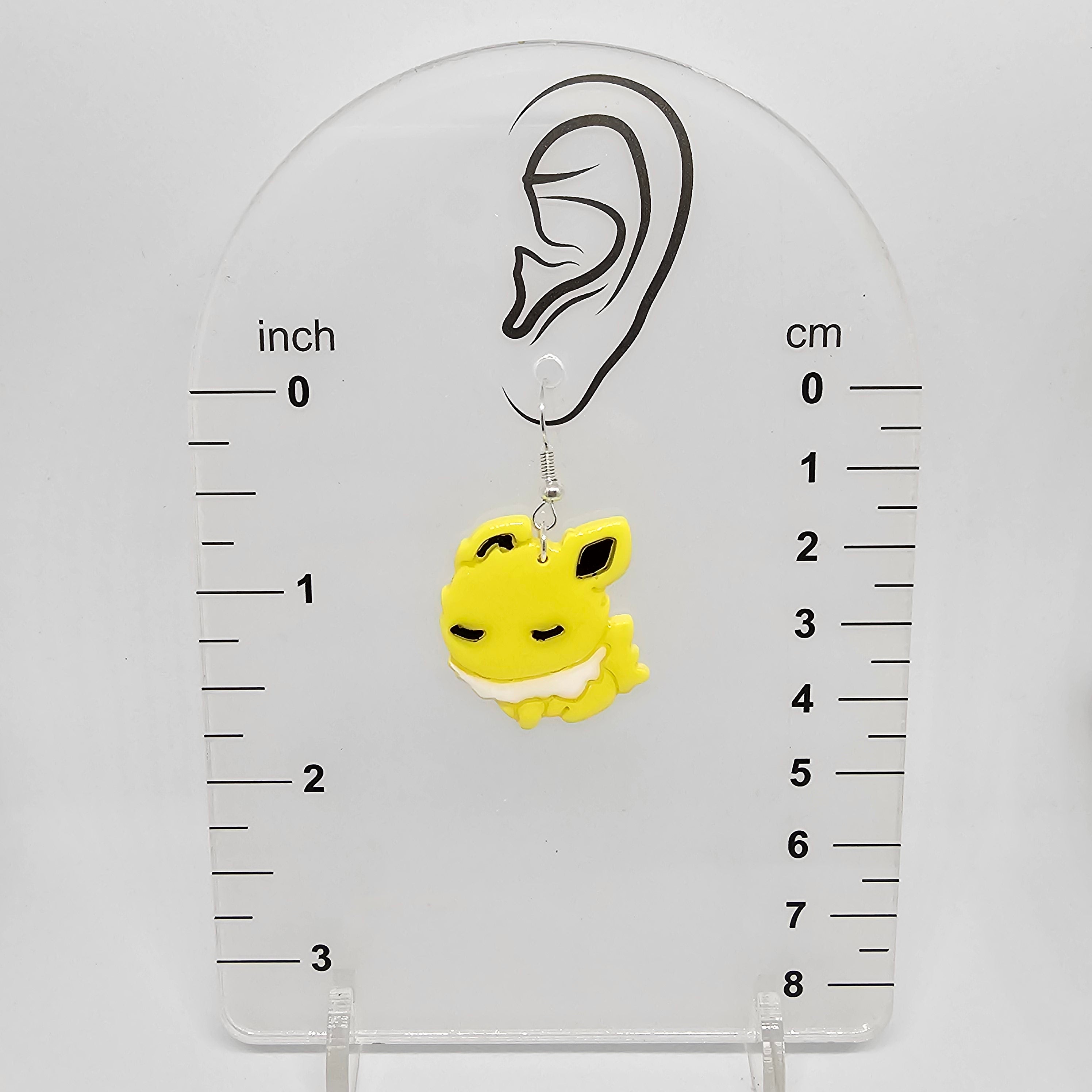 Jolteon earring on a measuring device showing it dangles 1.75in below the earring lobe hole.