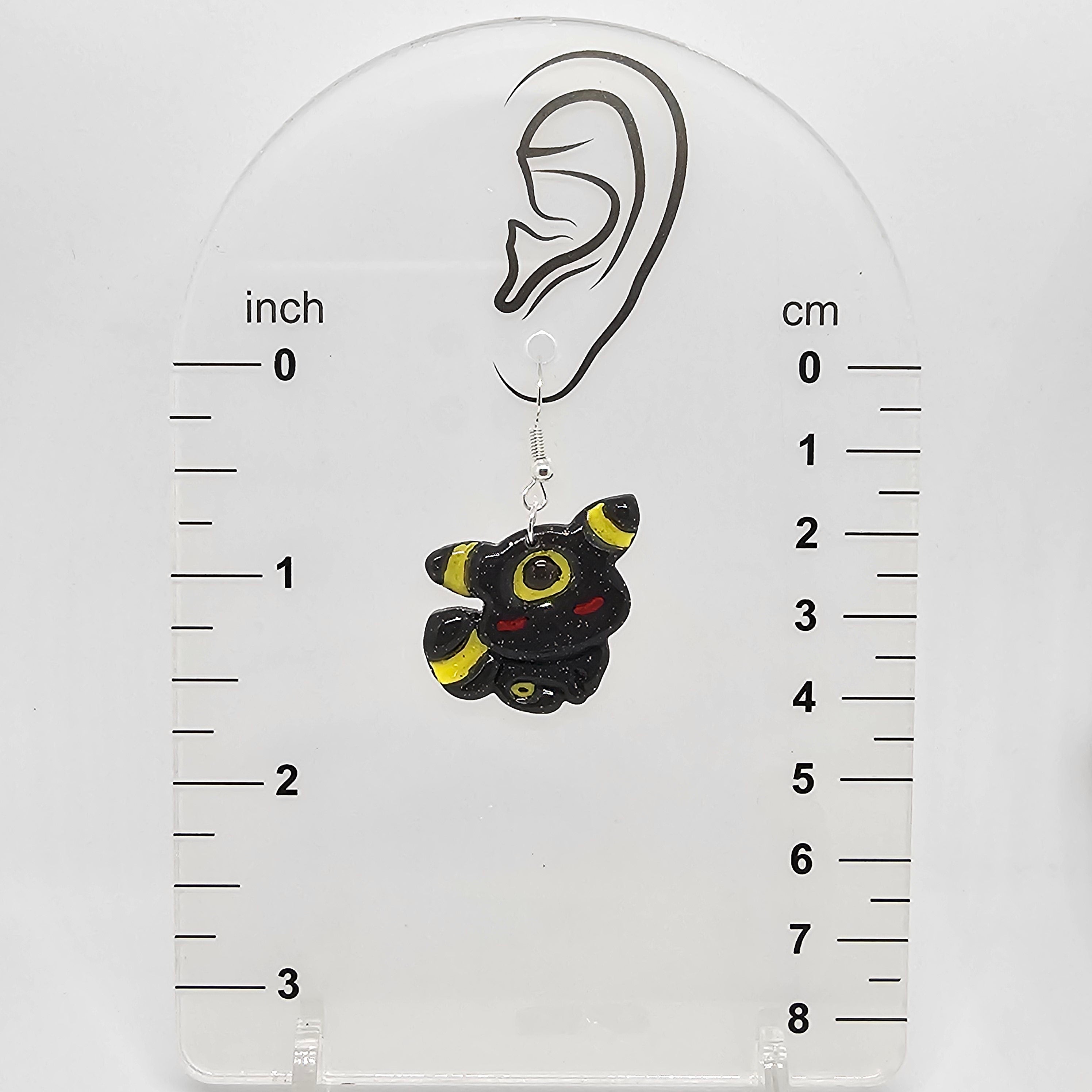 Umbreon earring hanging on a measuring device showing it dangles 1.75in from ear lobe hole. 