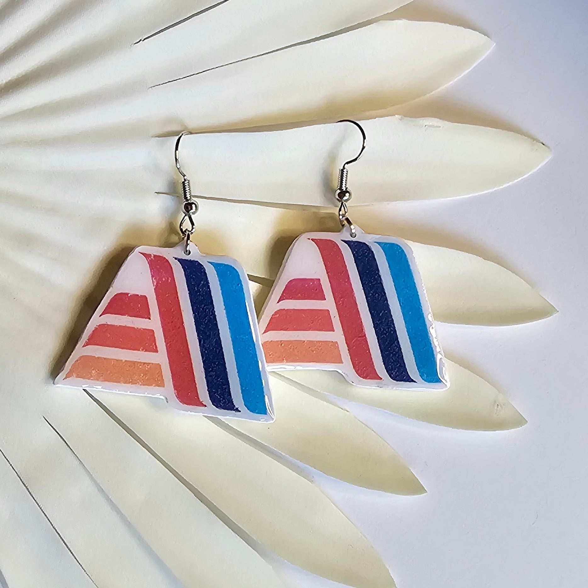 Silver dangle Aldi logo earrings made out of polymer clay hanging on a fern decoration. 